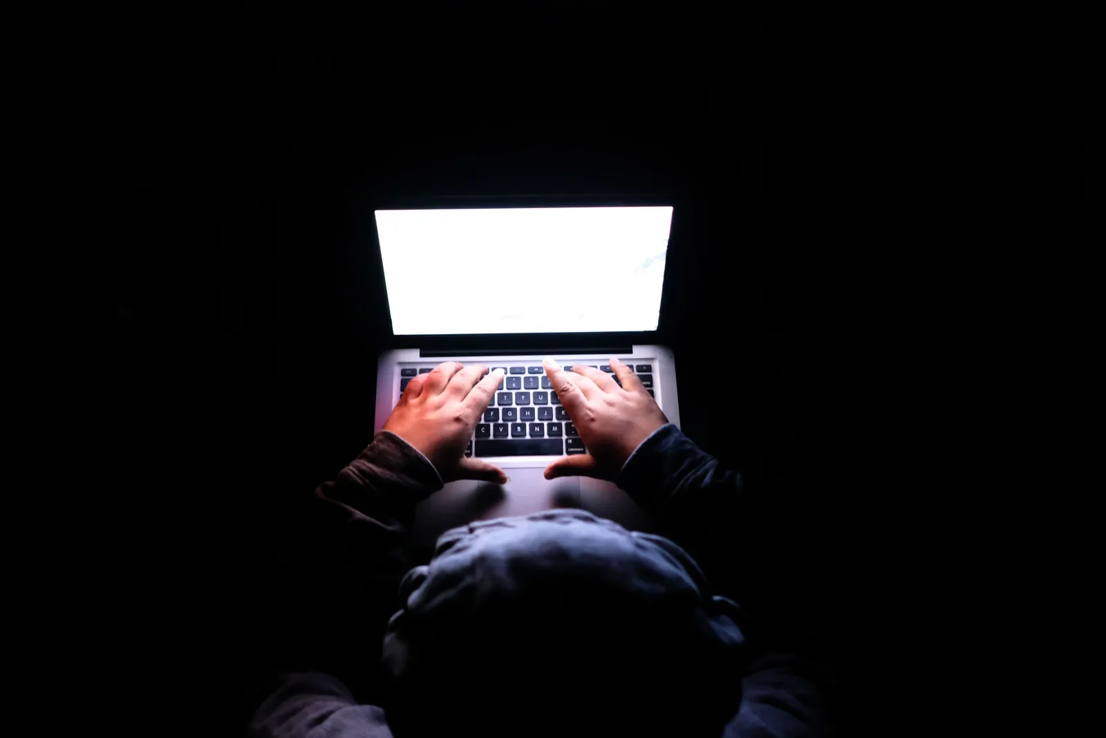 A person in a dark room typing on a laptop, symbolizing privacy, cybersecurity, and technology. Security warning signs on your devices, and what to do about them first