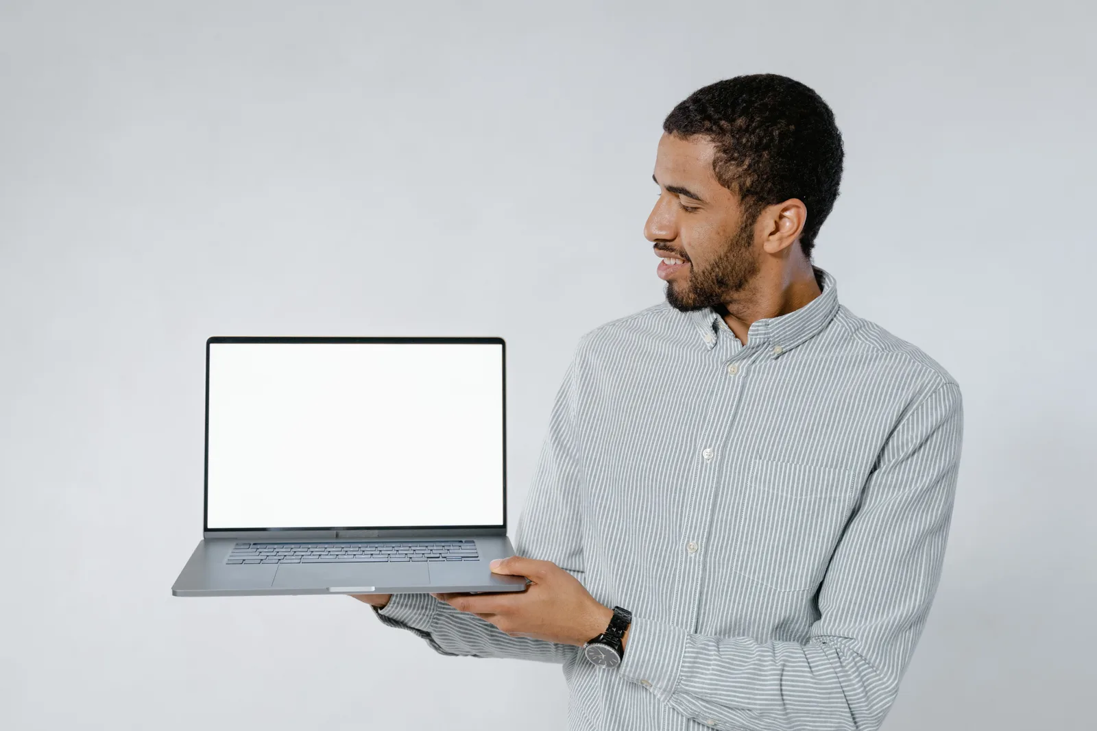 Man in striped shirt showcasing a laptop with blank screen against white background. Laptop replacement case: transfer, setup, retirement