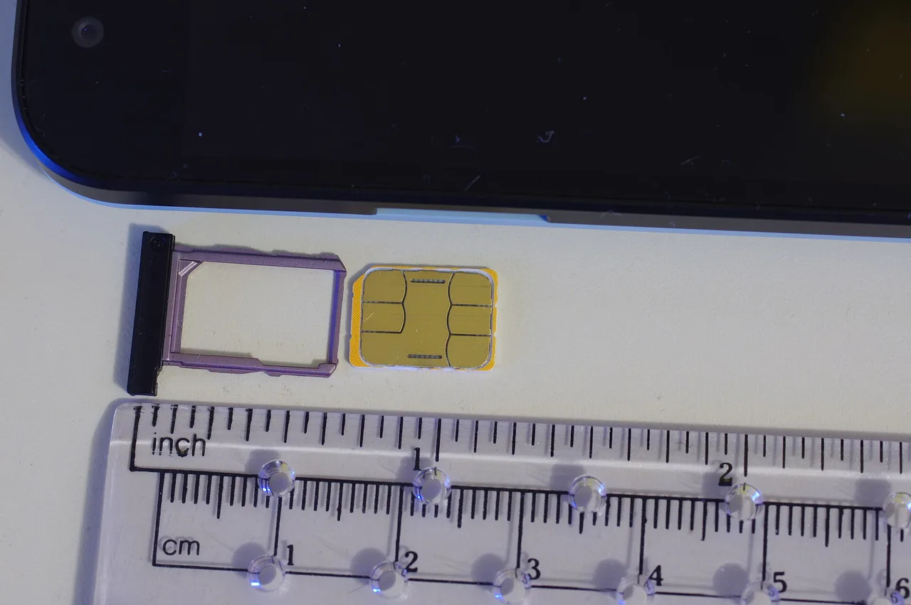 A nano SIM card beside its tray, a smartphone, and a ruler